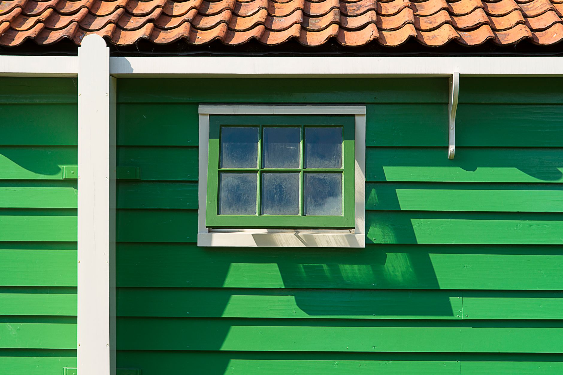 Close-up of a vibrant green wooden house with a small window and terracotta tile roof