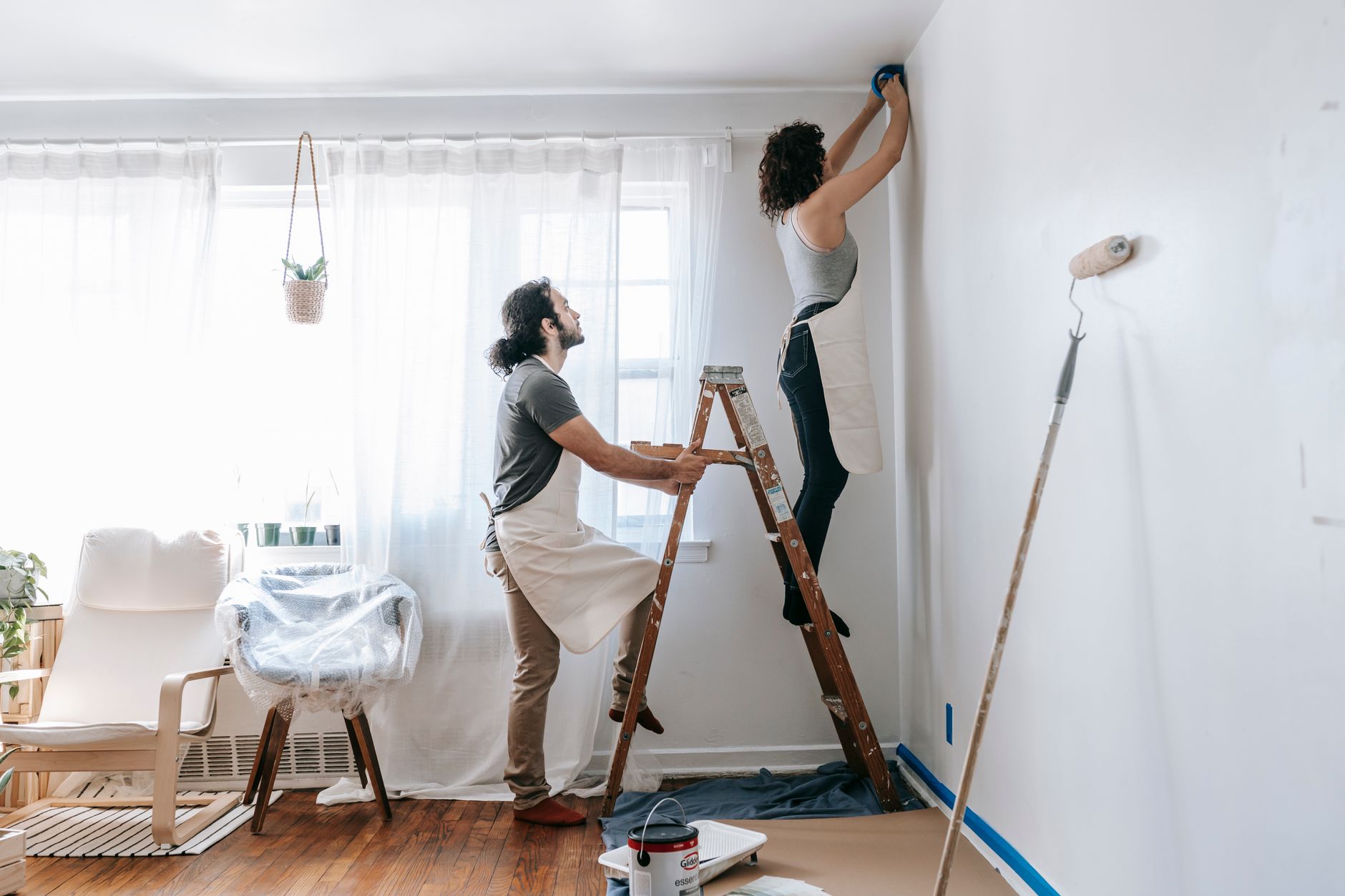 Couple renovating their home, with man supporting ladder and woman working on walls indoors